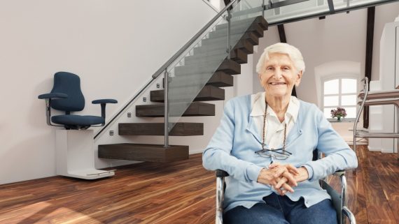 Seniorin im Rollstuhl vor Treppenlift zu Hause