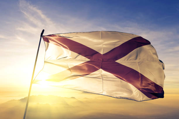 Alabama state of United States flag on flagpole textile cloth fabric waving on the top sunrise mist fog